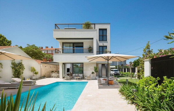A modern two-story house with a swimming pool, outdoor seating, and a balcony.