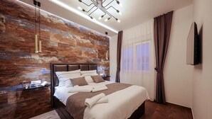 A modern bedroom with a large bed, a wooden accent wall, a mounted TV, and a ceiling light fixture.