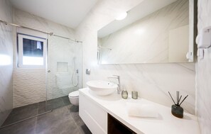 Un bagno moderno con cabina doccia in vetro, un lavandino bianco e uno specchio grande.