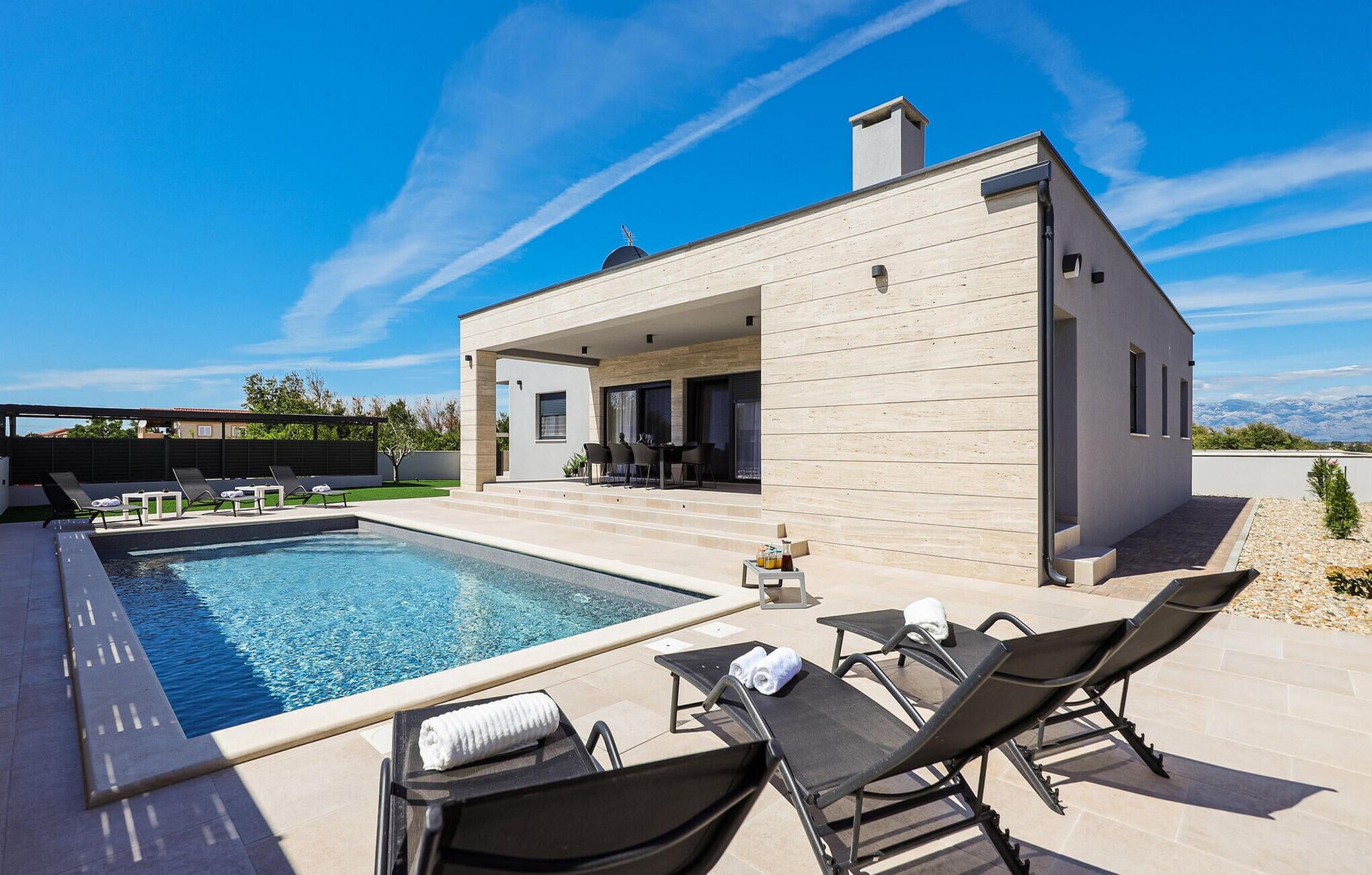 A modern house with a swimming pool, outdoor seating, and a view of the mountains.