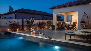 A swimming pool with a patio area, outdoor furniture, and a view of a house with a tiled roof. - Beautiful home in Nin (Nin)
