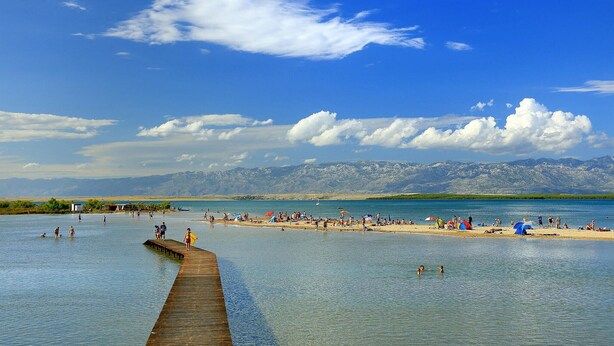 A beach with a wooden pier extending into calm waters, surrounded by mountains and clear skies. - Beautiful home in Nin (Nin)