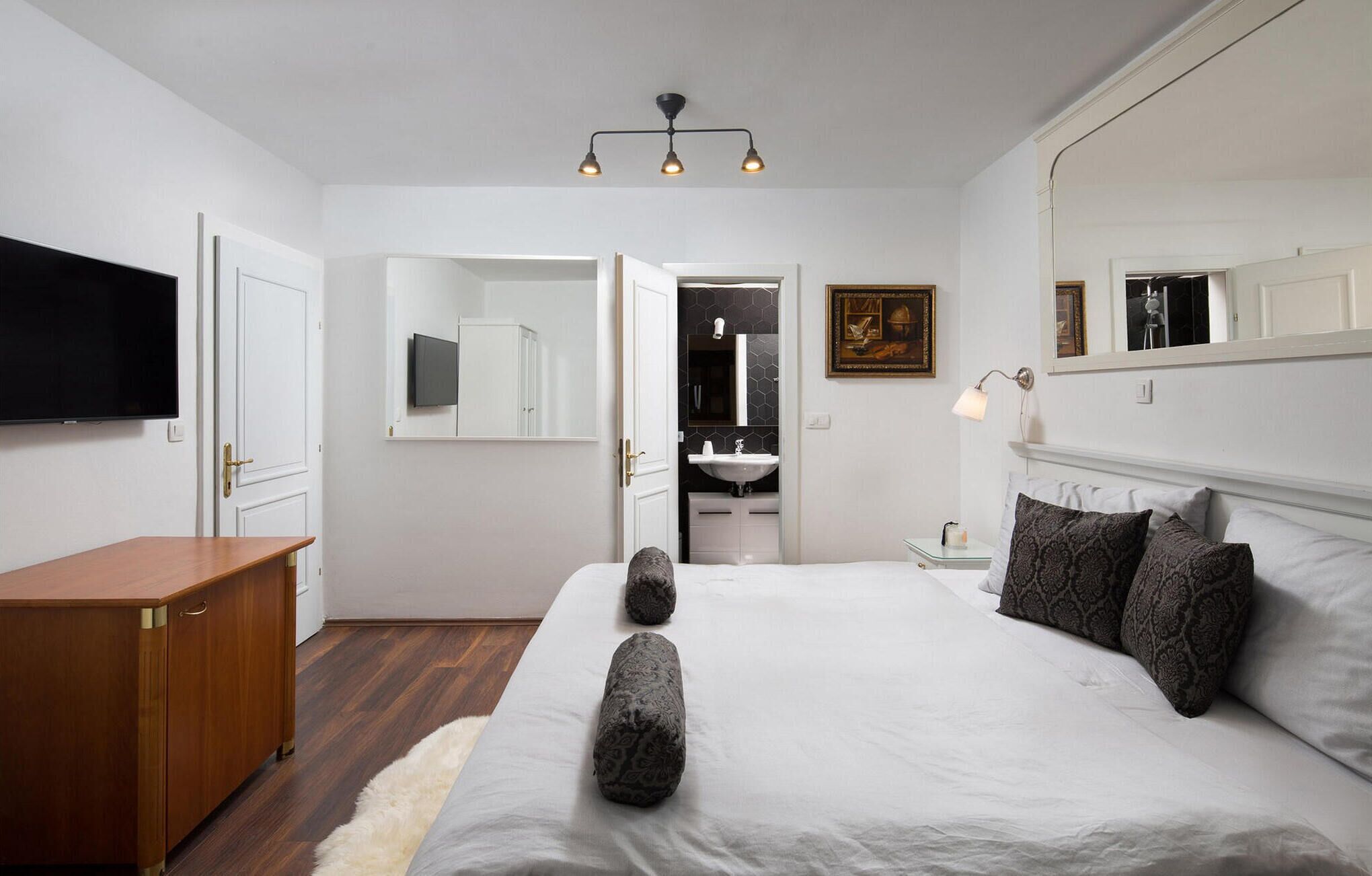 Een slaapkamer met een bed, nachtkastje en een aan de muur bevestigde televisie.