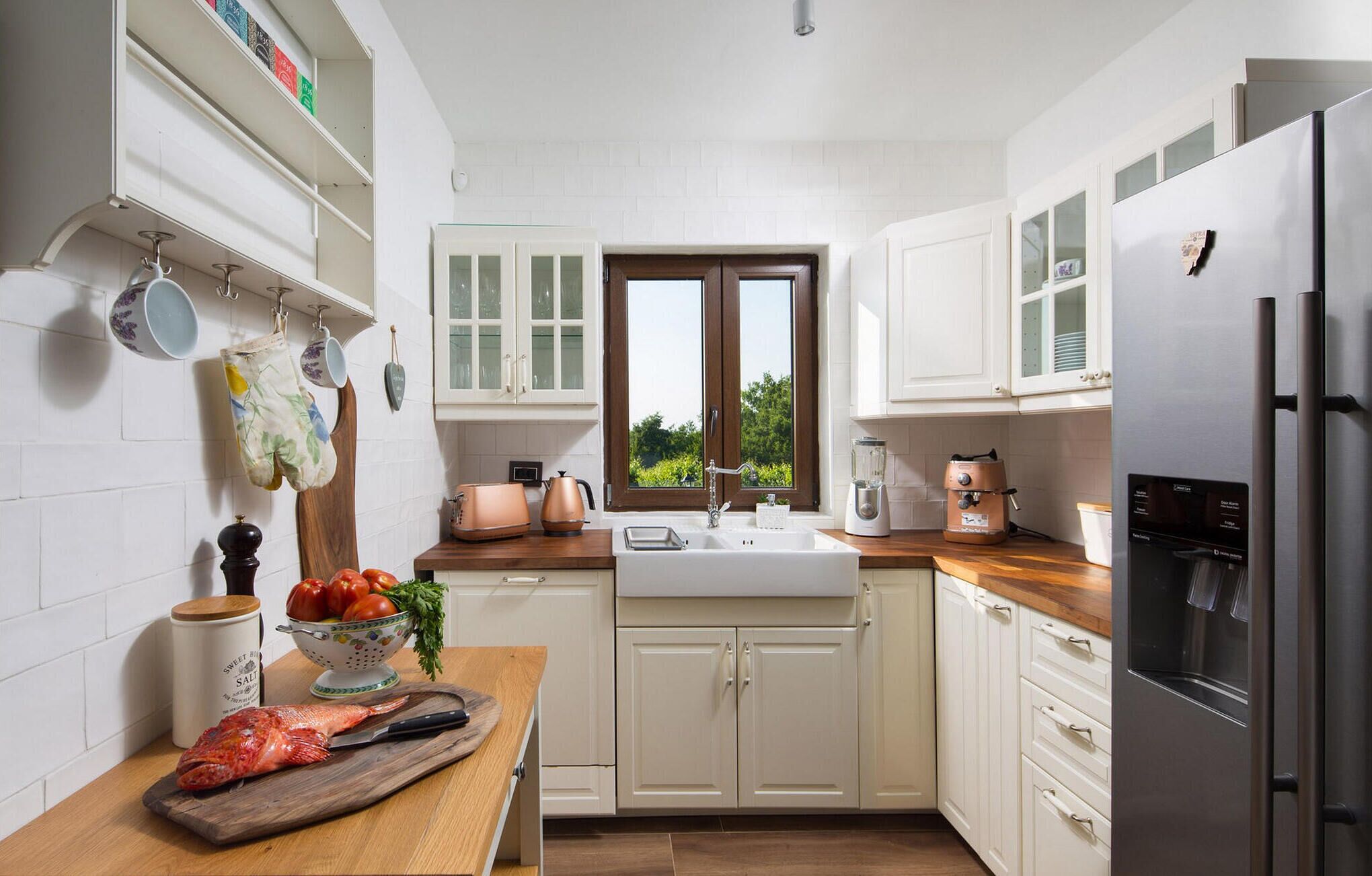 Una cucina moderna con mobili bianchi, un piano di lavoro in legno, un lavello, un fornello e un frigorifero.