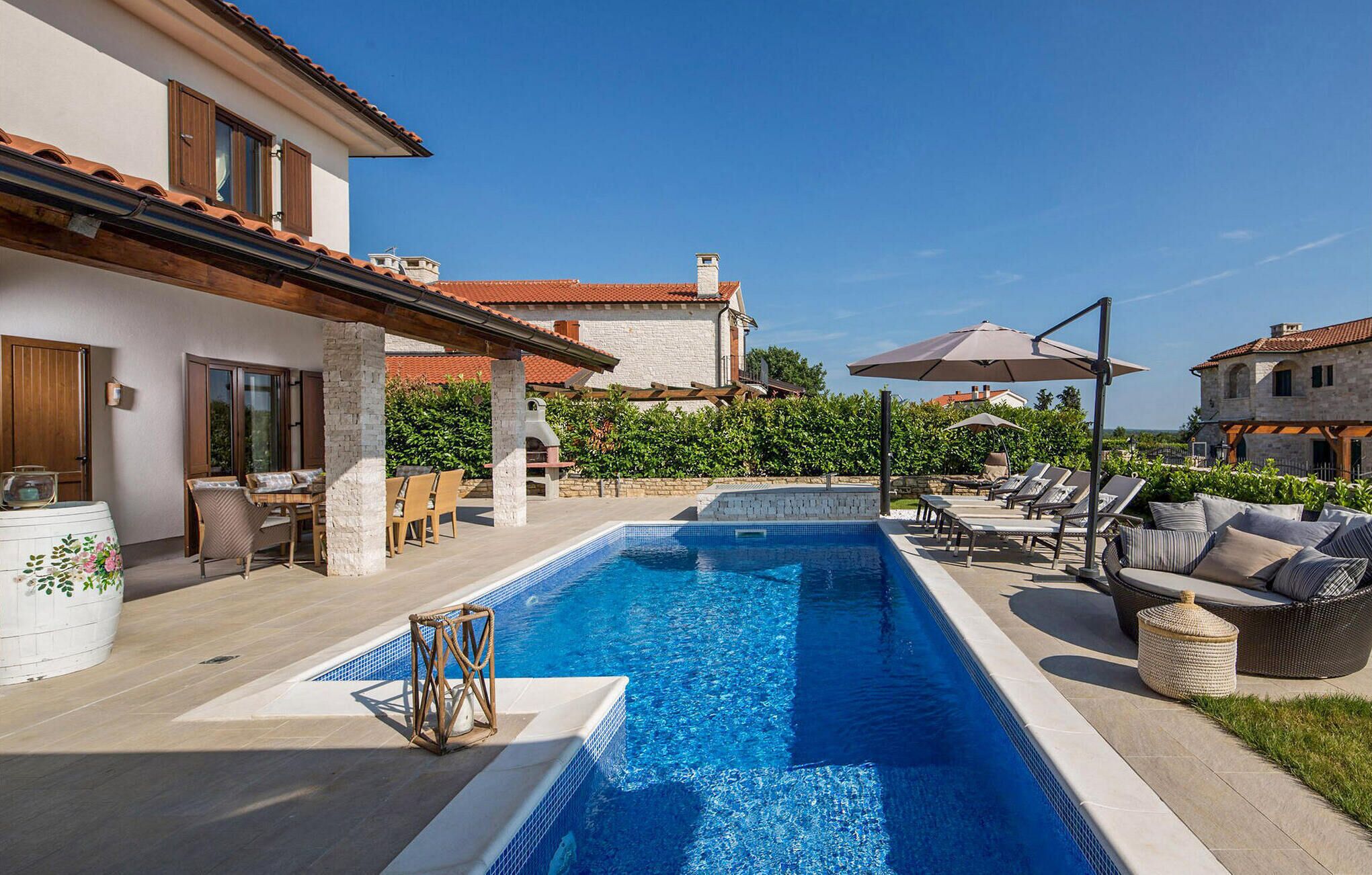 A swimming pool with lounge chairs and umbrellas, surrounded by stone buildings and greenery.