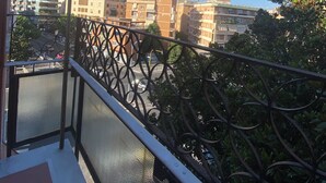 Un balcon doté d’une balustrade en métal, d’où l’on peut admirer un paysage urbain avec de nombreux immeubles et un ciel bleu dégagé.