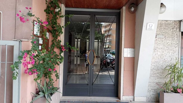 Une entrée d’immeuble avec une porte en verre, un portail en métal et un mur en briques.