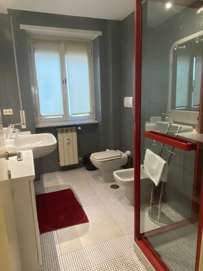 Een badkamer met een wit wastafel, toilet, bidet en douchehoek.