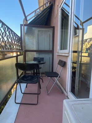 Een balkon met een tafel, twee stoelen, een glazen schuifdeur en een metalen hekwerk.