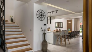 Un intérieur moderne comprenant un escalier, une grande horloge murale, un coin cuisine et un espace repas.