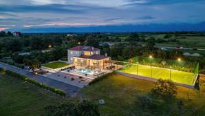 Une maison à deux étages avec une piscine et un court de tennis.