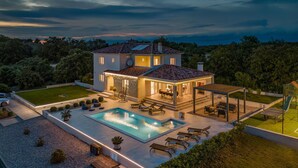 Una casa de dos pisos con piscina, mobiliario exterior y un césped bien cuidado.