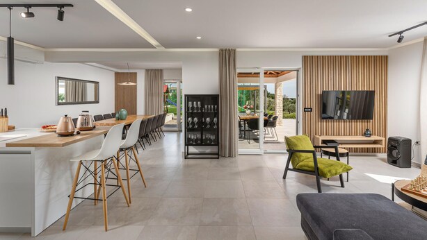 Una cocina moderna con una isla central, una zona de comedor con una mesa larga y un espacio de sala de estar con televisión y asientos.