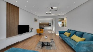 Una sala moderna con televisor de pantalla plana, un sofá, una mesa de centro y un comedor al fondo.