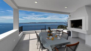 Un balcón con una mesa dispuesta para el desayuno, con vistas a un paisaje marino y colinas a lo lejos.