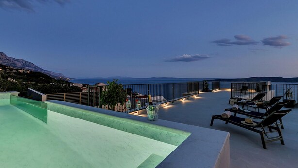 Una terraza en la azotea con piscina, sillones de descanso y vistas al mar y a las montañas.