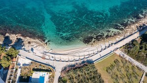 Vista aérea de una propiedad costera con una carretera sinuosa, una piscina y un litoral rocoso.