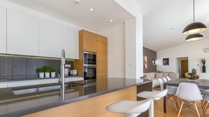 A modern kitchen with a central island, built-in appliances, and a dining area with a long table and white chairs. - 5 bedroom gorgeous home in Hvar (Hvar)