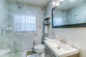 Une salle de bain moderne avec un mur en marbre, un lavabo blanc et un grand miroir.