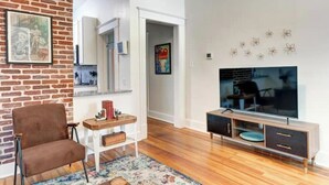A living room with a brick wall, a brown chair, a TV stand, and a rug. - Tucked Inn fantastic location! (Memphis)