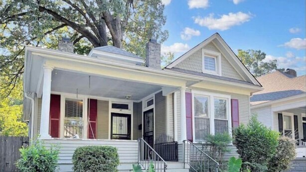 A two-story house with a front porch, a chimney, and a small front yard with a few shrubs. - Tucked Inn fantastic location! (Memphis)