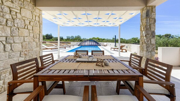 Ein Poolbereich im Freien mit Holztisch und -stühlen, Steinmauern und Blick auf den Pool.