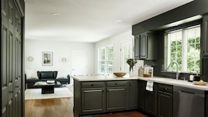 Une cuisine moderne avec des meubles de couleur sombre, un grand îlot central et une vue sur l’extérieur grâce à une fenêtre.