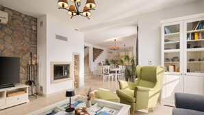 Un amplio salón con pared de piedra, chimenea, televisor, zona de comedor y estantería.