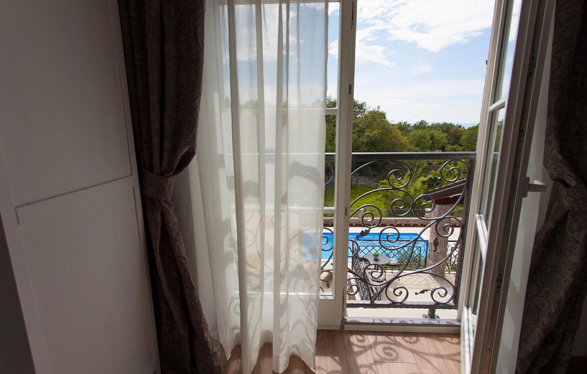 An open balcony door with a view of a pool and greenery.