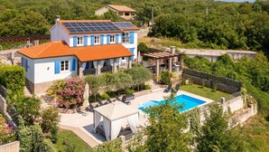 Una casa de dos pisos con piscina, paneles solares y jardín.