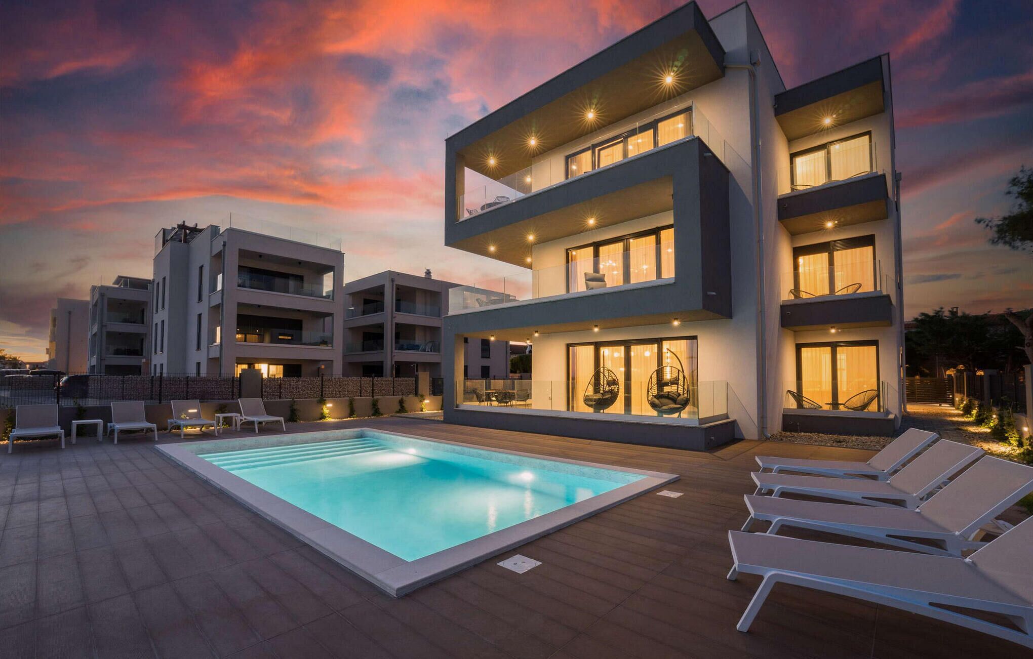 A modern multi-story building with a rooftop pool and lounge chairs.