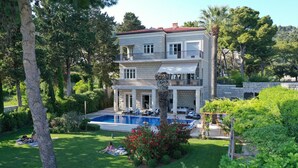 A two-story building with a swimming pool, surrounded by lush greenery and trees.