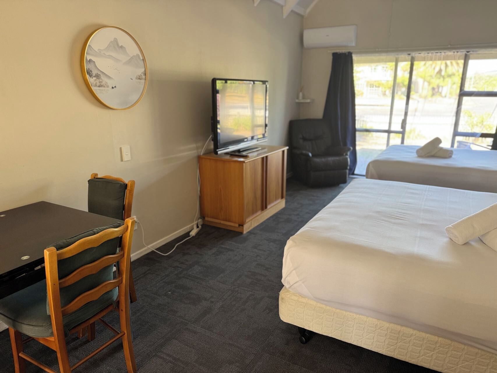Een hotelkamer met een bed, een bureau met stoel, een televisie en een raam met gordijnen.