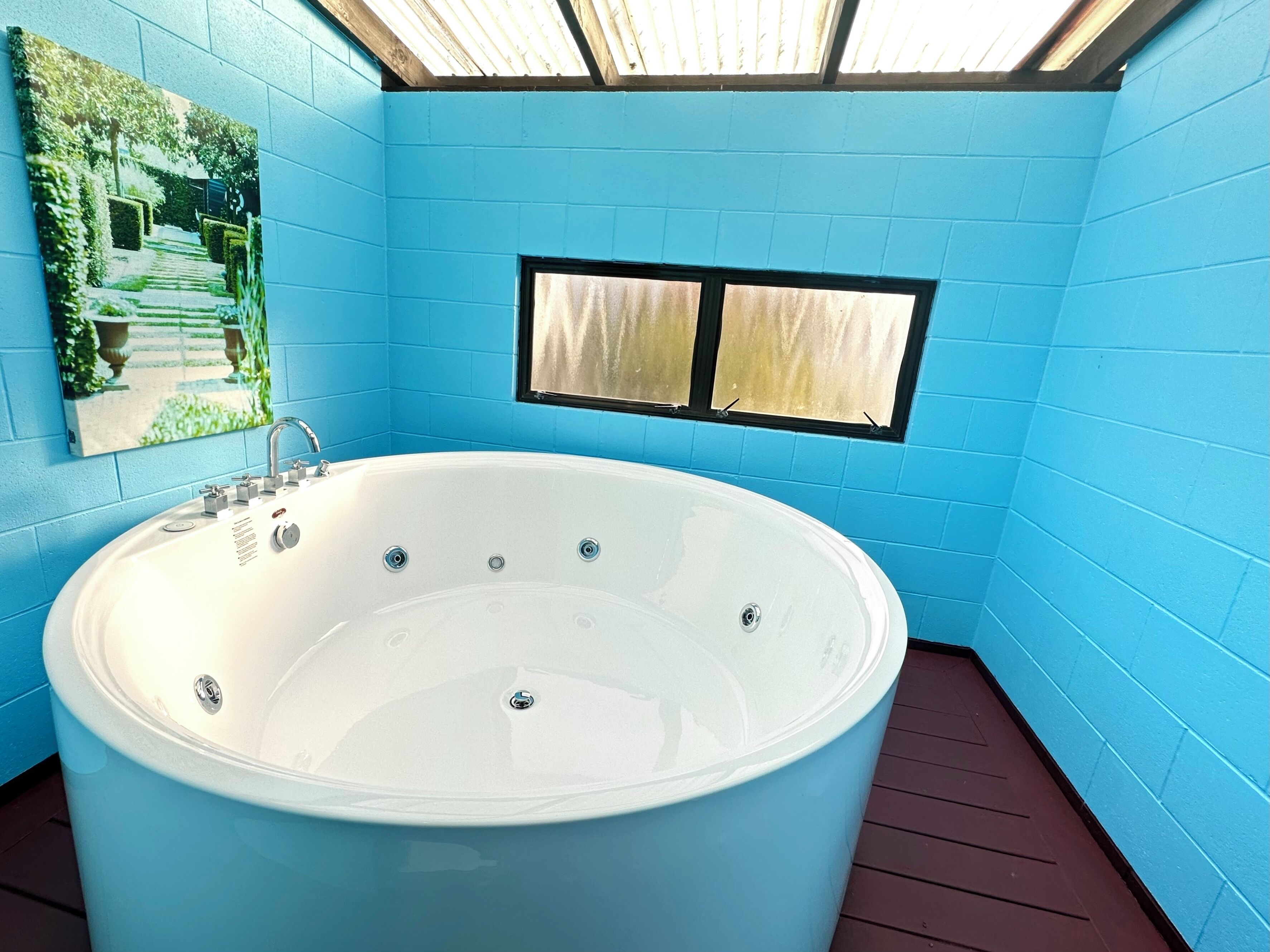 A modern bathroom with a large bathtub, blue walls, a skylight, and a window.