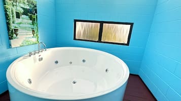 A modern bathroom with a large bathtub, blue walls, a skylight, and a window.