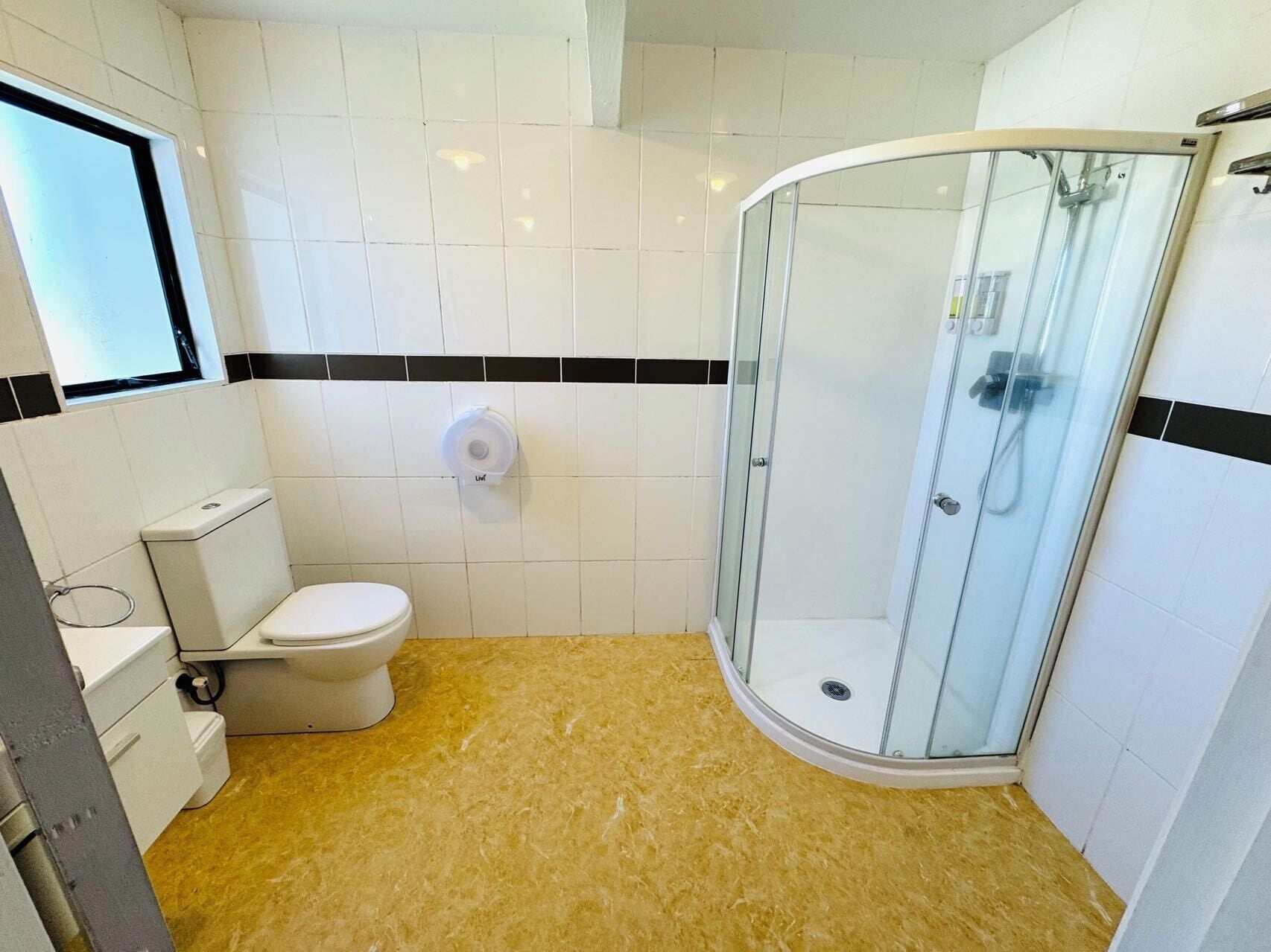 A bathroom with a toilet, a glass shower enclosure, and a toilet paper holder on the wall.