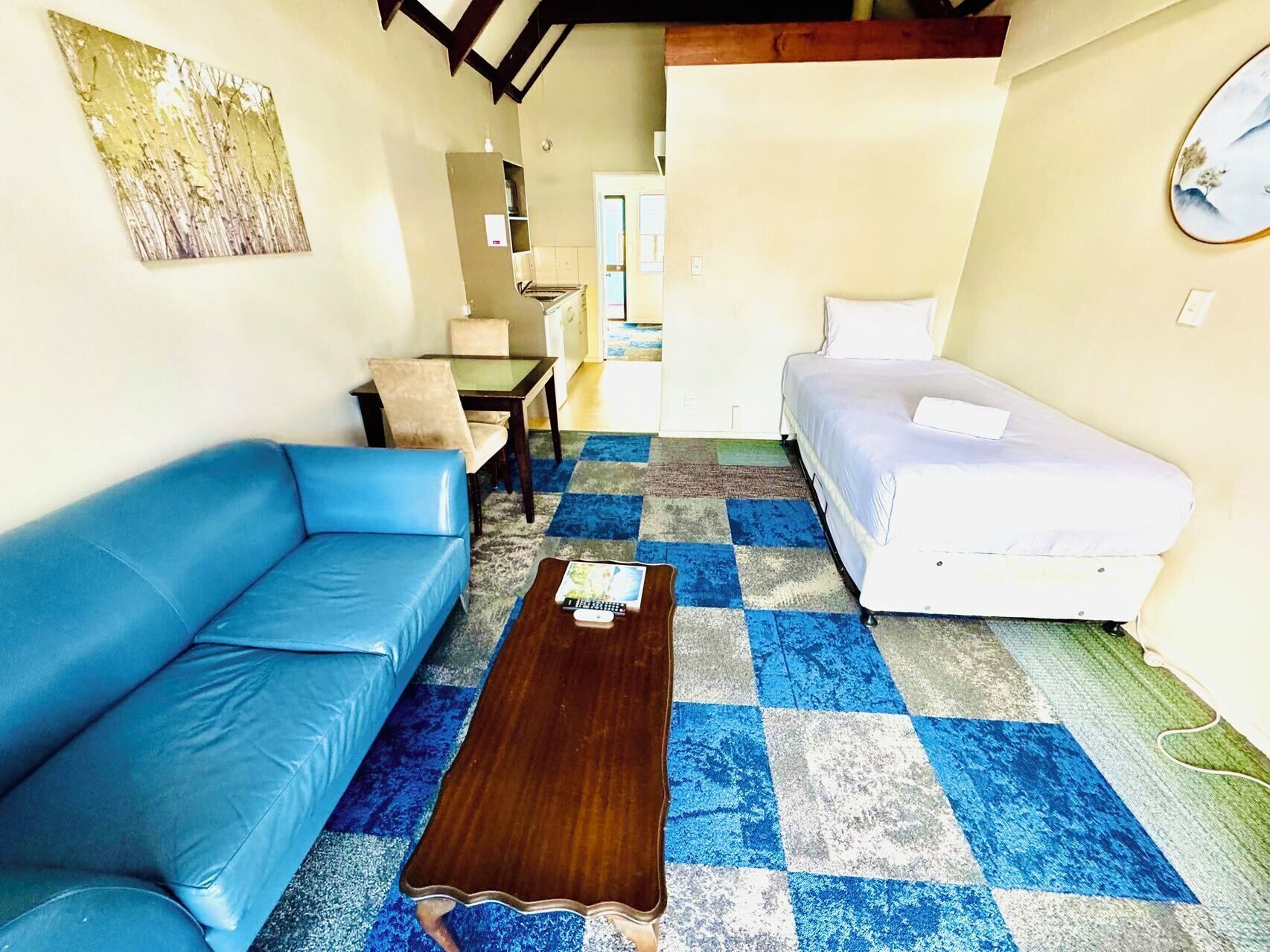 Una stanza accogliente e piccola con un divano blu, un letto bianco e un tavolino in legno.