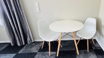 A room with a checkered carpet, a white round table, and two white chairs with wooden legs.