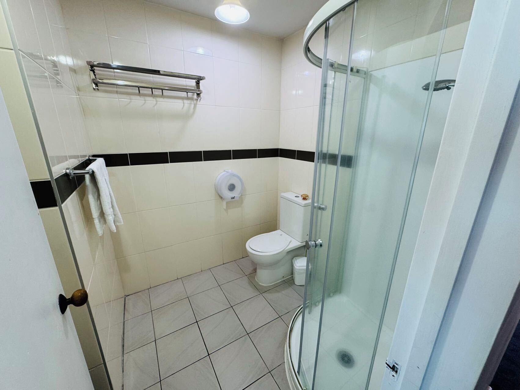 A bathroom with a toilet, a glass shower enclosure, a towel rack, and a paper towel dispenser.
