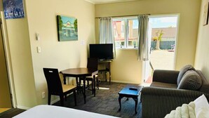 A hotel room with a bed, a TV, a dining table with chairs, a sofa, and a window with curtains. - Apex on Fenton (Rotorua)