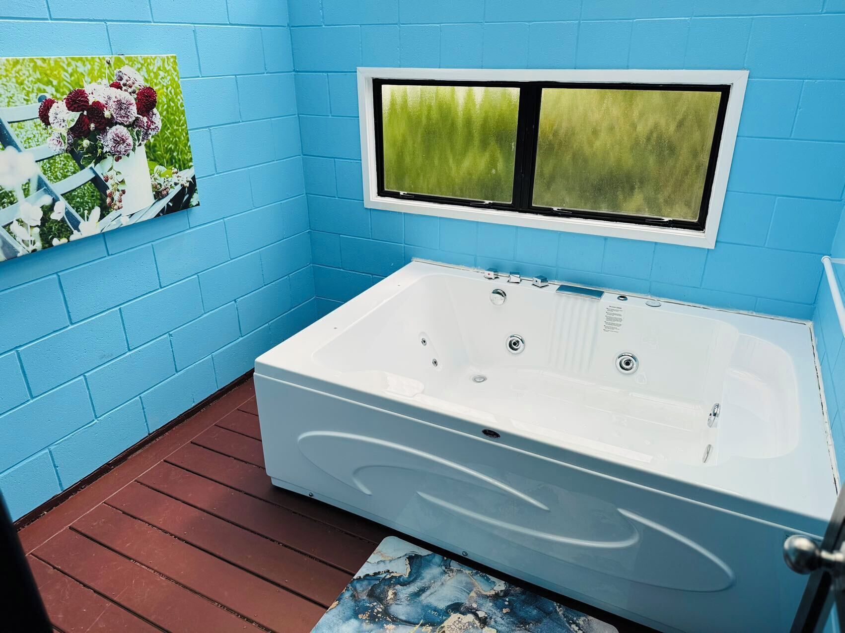 A bathroom with a white bathtub, blue walls, and a window with a green view.