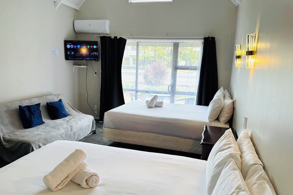Habitación de hotel con dos camas, un sofá, un televisor y una ventana con cortinas.