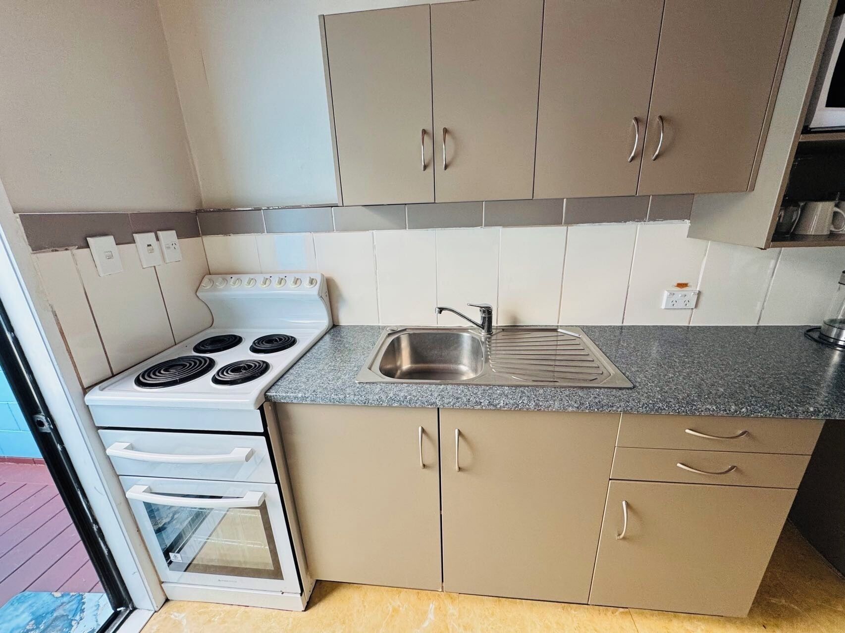A compact kitchen with a white stove, a sink, and beige cabinets.