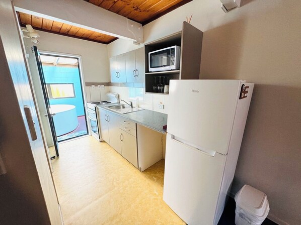 A compact kitchen with white appliances, including a refrigerator, microwave, and stove. - Apex on Fenton (Rotorua)
