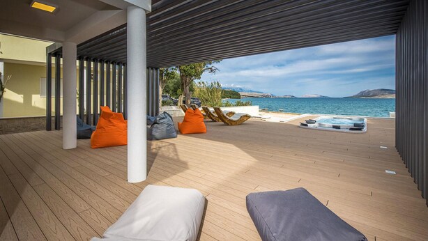 A covered outdoor area with wooden flooring, orange and gray bean bags, and a hot tub overlooking a body of water. - Lovely home in Novalja with WiFi (Novalja)
