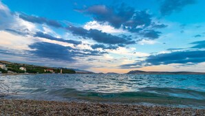 A coastal landscape with a pebbly beach, calm sea, and distant mountains under a partly cloudy sky. - Lovely home in Novalja with WiFi (Novalja)