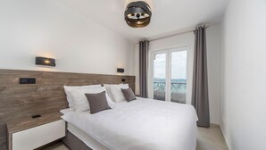 A modern bedroom with a wooden headboard, a large bed with white linens, two bedside tables, and a view of the sea through a balcony. - Lovely home in Novalja with WiFi (Novalja)