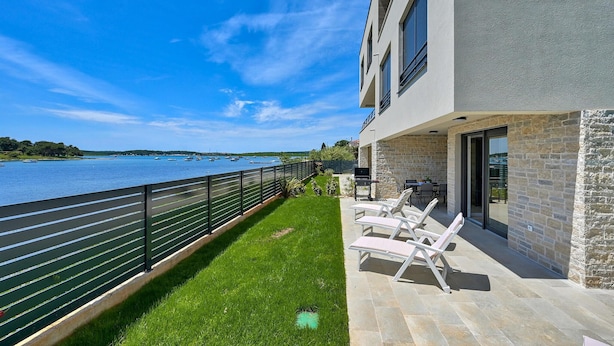Ein modernes Gebäude mit einem Balkon mit Blick auf ein Gewässer, ausgestattet mit Sitzgelegenheiten im Freien und einer Grillzone.