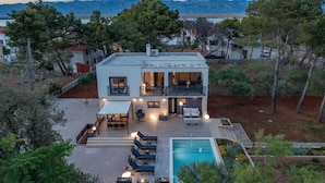 A two-story house with a pool, outdoor seating, and a view of the mountains.