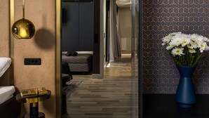 A modern hotel room with a wooden floor, a bed with white linens, a blue vase with white flowers, and a patterned wall.